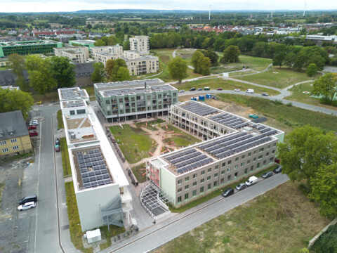 Das Bild zeigt eine Luftbildaufnahme aus geringer Höhe mit Blick über den vierseitigen Block des Grünen Weilers in Richtung Süden mit dem charakteristischen grünen Baukörper des vom-Stein-Gymnasiums im Mittelgrund links und den baumbestandenen Grünanlagen Grüner Trichter/Grüner Finger, die sich in Richtung Horizont ziehen. 