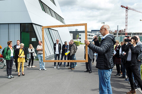 Bei dem Zukunftsspaziergang in den urbanen Wissensquartieren hält Marc Günnewig symbolisch einen Holzrahmen hoch, um neue Perspektiven für diesen Ort zu zeigen.