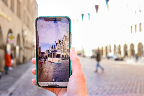 Das historische Münster als Smartphone App. Hier fährt mit Hilfe von Augmented Reality auf dem Prinzipal­markt die historische Straßen­bahn auf die Betrachter*innen zu.